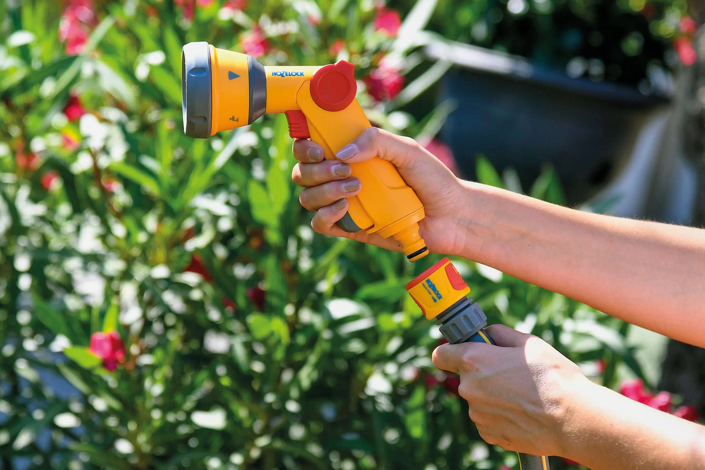 The Multi Spray Soft Touch Gun offers unparalleled comfort and water-saving efficiency for your garden watering needs. Person holding a yellow garden hose nozzle with a blurred garden background