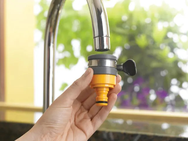 Hand holding a yellow and black Hozelock faucet adapter against a blurred outdoor background [ Davies DIY ]