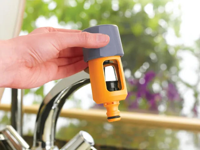 Hozelock Mixer Tap Connector Hand holding a yellow and gray faucet adapter with a blurred outdoor  [ Davies DIY & Builders Supplies ]background