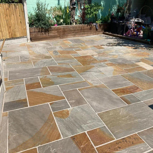 Garden patio laid with mixed-size Two Tone natural sandstone paving slabs in blue-grey, bronze and earthy brown colours.